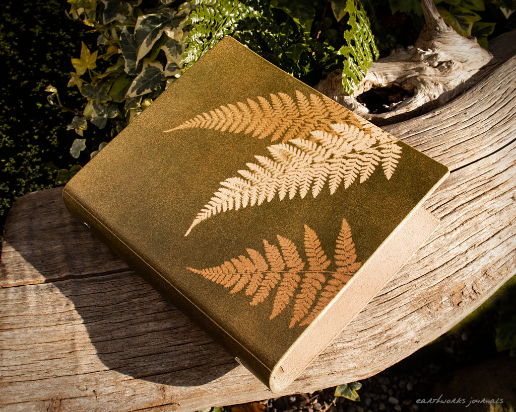 A5 leather 6 ring binder with fern leaf design on a weathered piece of wood. made by earthworks journals
