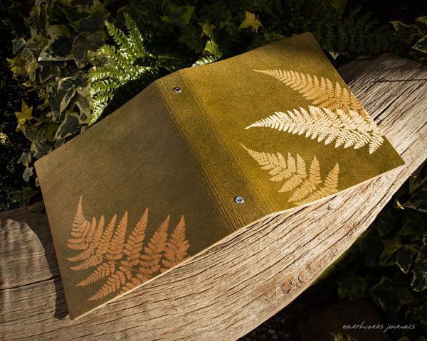 A5 leather 6 ring binder with fern leaf design on a weathered piece of wood. made by earthworks journals