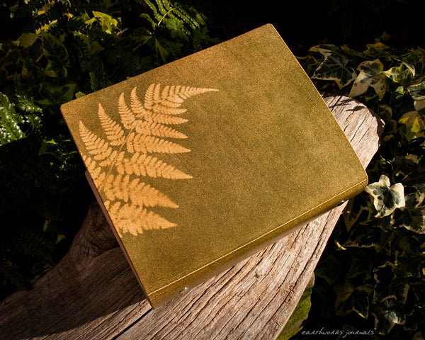 A5 leather 6 ring binder with fern leaf design on a weathered piece of wood. made by earthworks journals