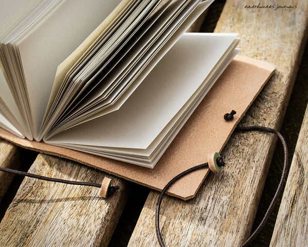 a small  open leather journal on a piece of weathered wood, made by earthworks journals