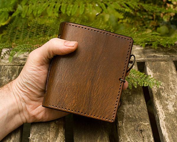 small brown leather journal being held in a hand, made by earthworks journals