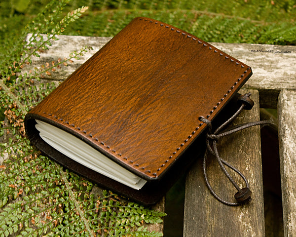 small brown leather journal surrounded by fern leaves, made by earthworks journals