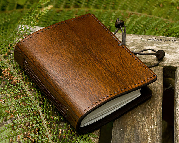 small brown leather journal surrounded by fern leaves, made by earthworks journals