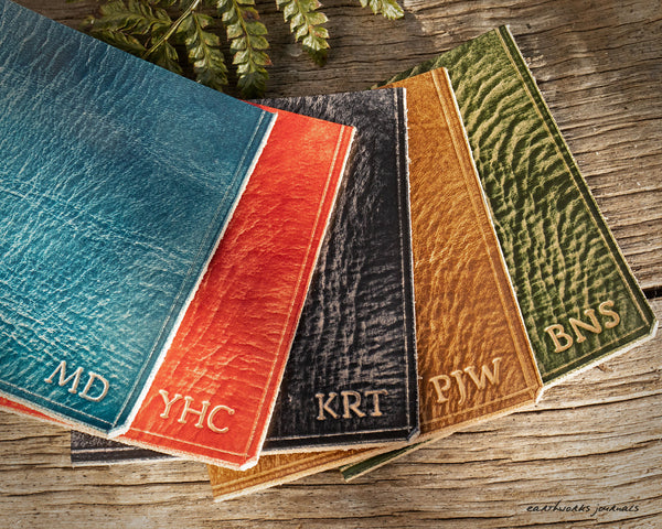 Five coloured pieces of leather showing examples of tooled personalisation - earthworks journals
