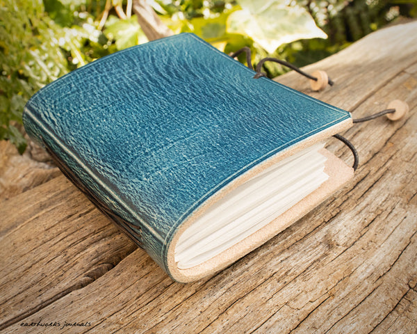 a small blue leather notebook on a piece of weathered wood, made by earthworks journals